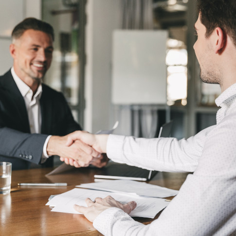 Business, career and placement concept - successful young man smiling, and handshaking with european businessman after successful negotiations or inte